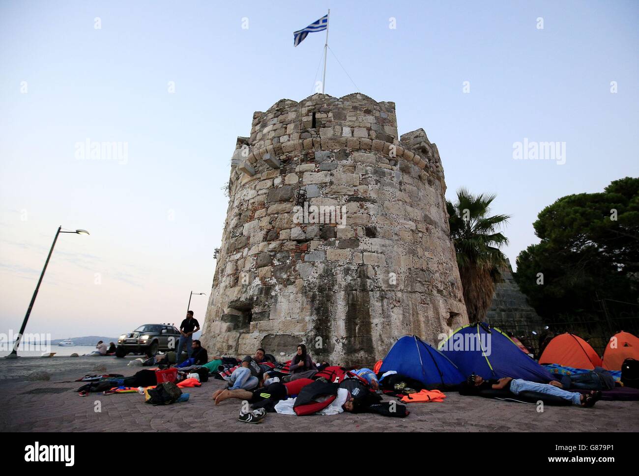 I migranti e i rifugiati si riuniscono tra le tende ai piedi di un'antica battaglia presso il porto dei traghetti di Kos, Kos, Grecia. Foto Stock