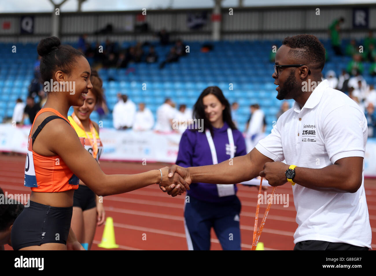 Il mentore di un atleta distribuisce la medaglia d'argento a Sharhnee Skervin per le ragazze a 100 metri durante i Sainsbury's 2015 School Games alla Manchester Regional Arena. Foto Stock