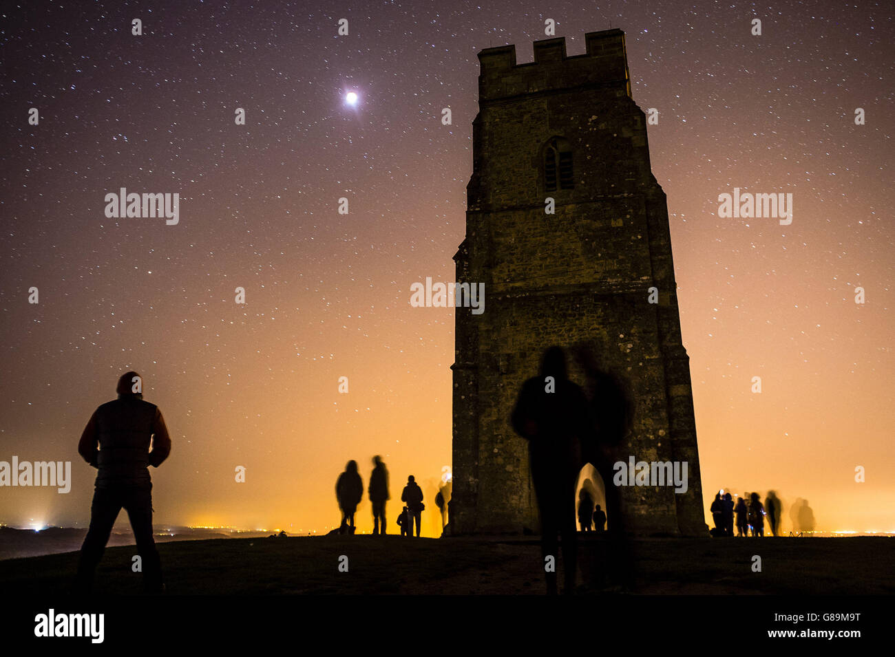 La gente guarda una 'supermoon' dalla cima di Glastonbury Tor mentre l'ombra della terra copre completamente la luna luminosa creando un'eclissi totale. Foto Stock