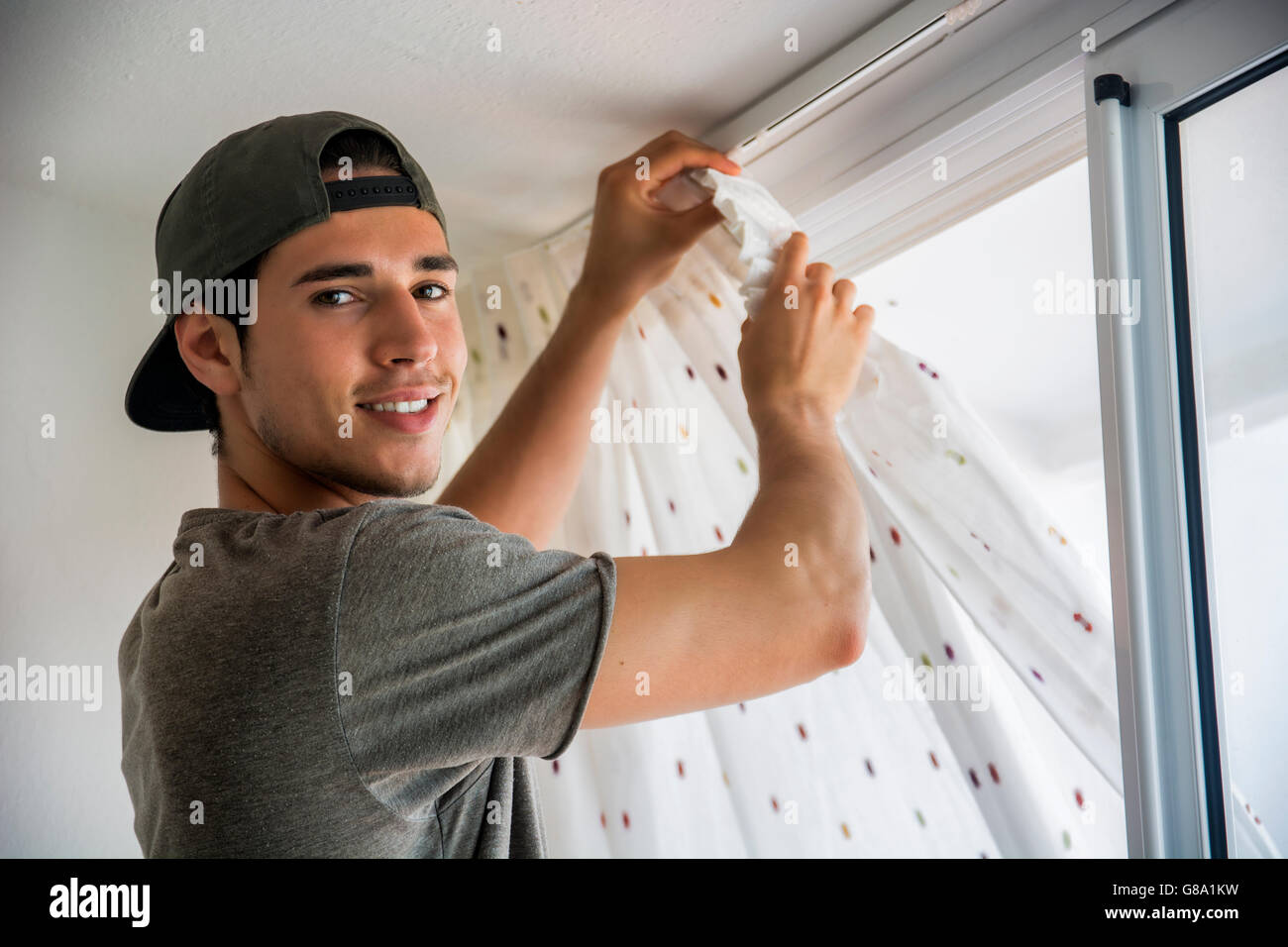 Giovane uomo bello o tuttofare installazione tende alle finestre di casa, facendo lavori di rinnovo Foto Stock
