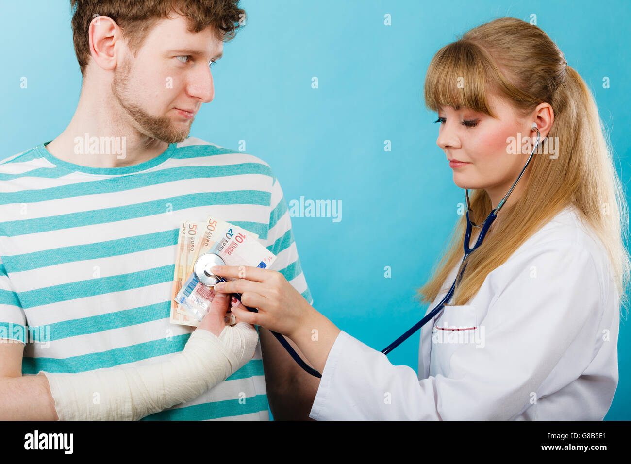 La corruzione in medicina. Medico donna con uno stetoscopio controllo del battito cardiaco. Maschio a mano bendato con banconote euro di denaro. Foto Stock