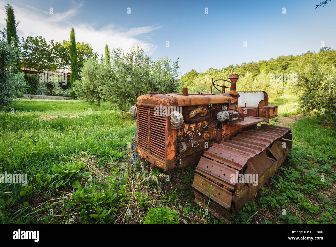 Il vecchio trattore arrugginito trascurato sotto l'albero Foto Stock