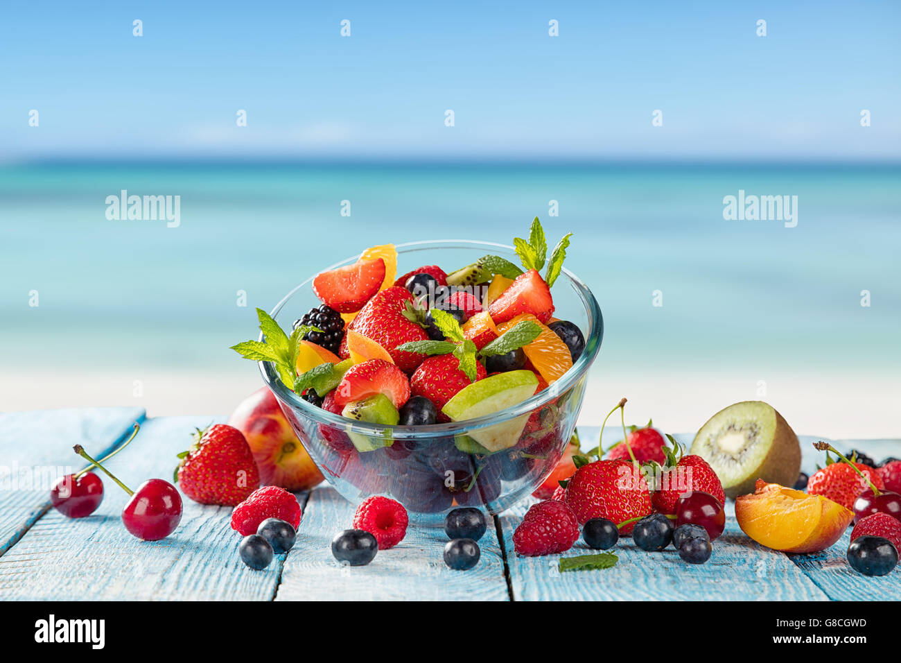 Insalata di frutta fresca posto su assi di legno, mare di sfocatura sullo sfondo. Concetto di mangiare sano, antiossidanti e l'estate. Foto Stock