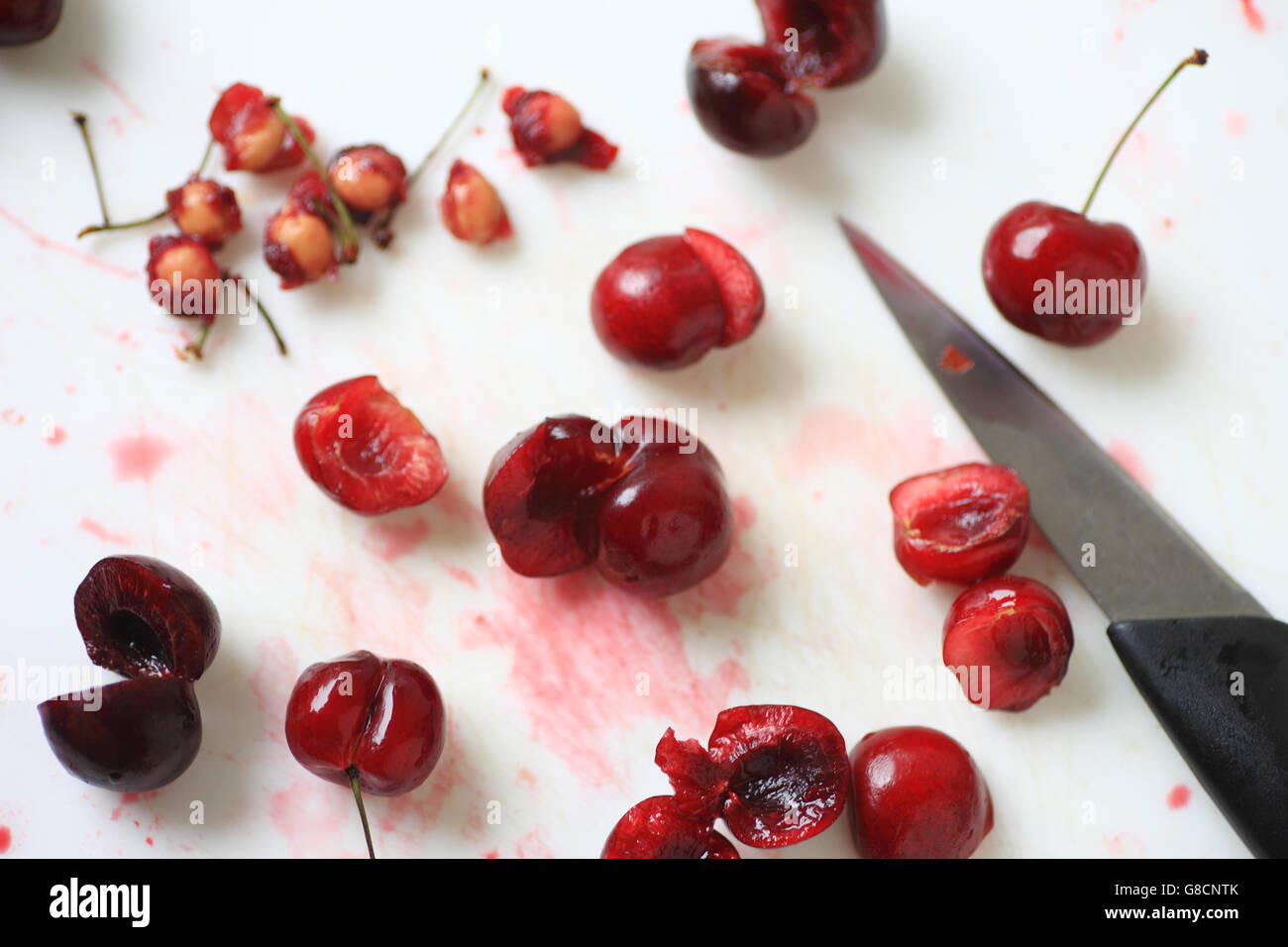 Fresche ciliege rosse, alcuni interi, altri snocciolate con pila di box e coltello seghettato Foto Stock
