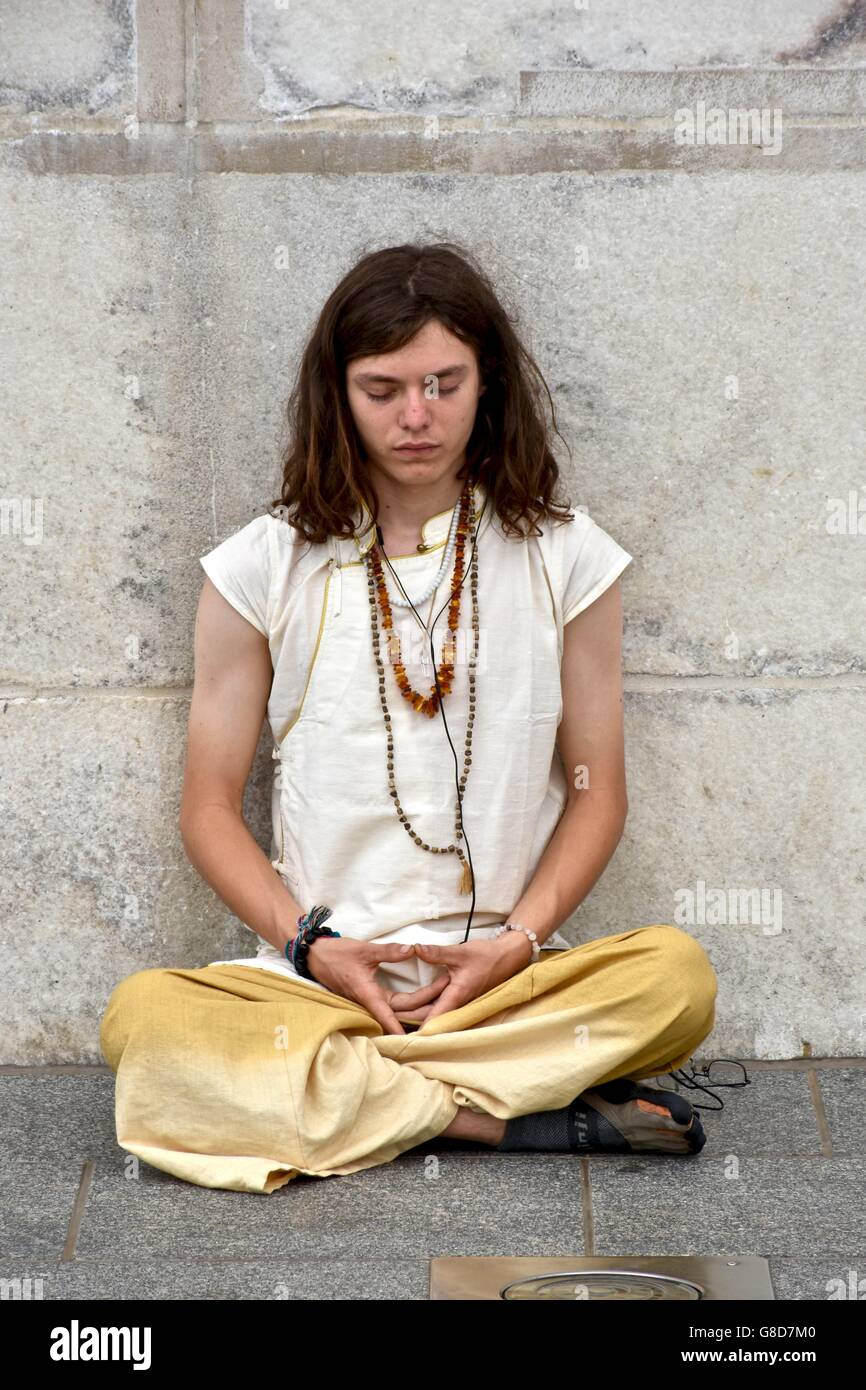 Un uomo che fa una meditazione spirituale mentre seduto contro il Washington Monument in c.c. Foto Stock