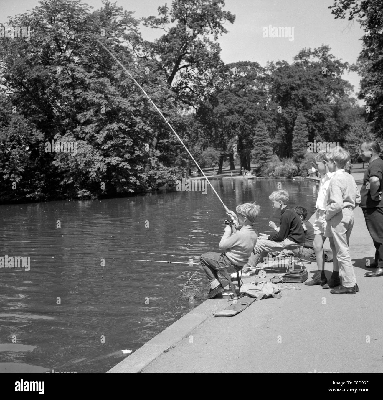 I giovani pescatori - in vacanza dalla scuola - trattengono il respiro con l'emozione di catturare un pesce al lago nel parco di Raphael, Romford, Essex. Foto Stock