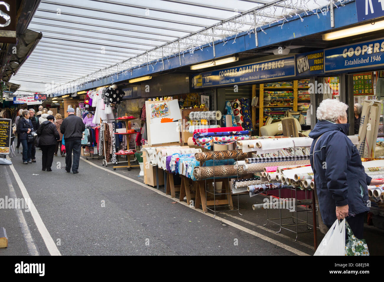 Una sezione di copertura di Bury Mercato, Greater Manchester con capi di abbigliamento in tessuto e bancarelle. Foto Stock