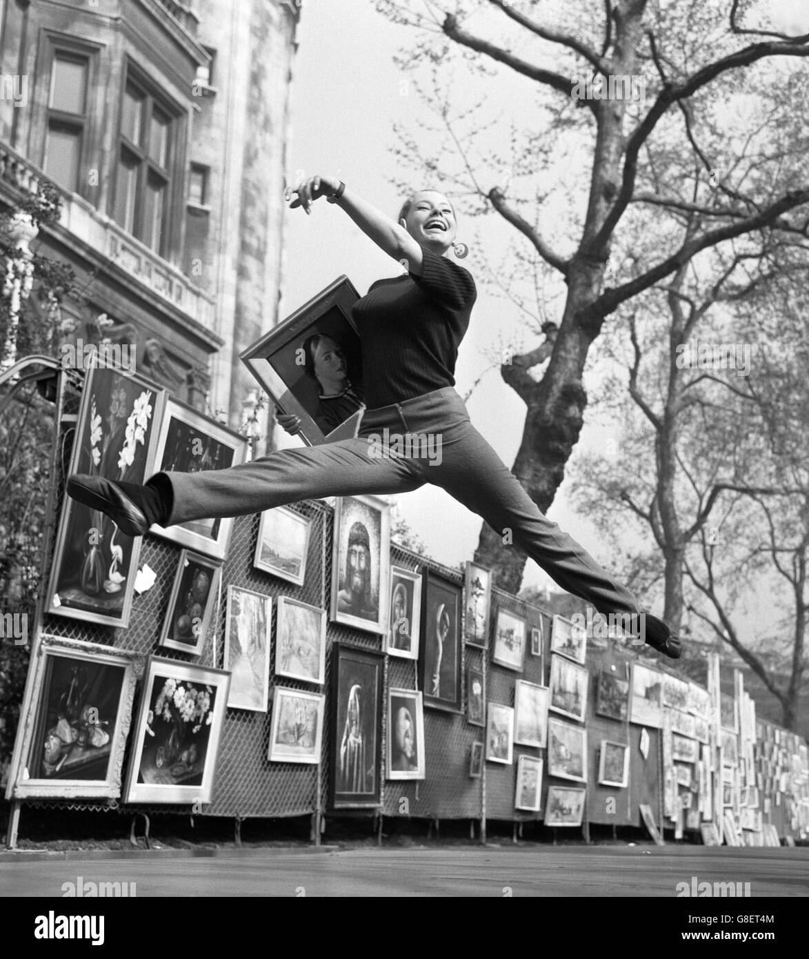 La studentessa di danza Wanda Bailey, 15 anni, di Brighton, compie un salto mentre porta uno dei dipinti del padre in una mostra d'arte all'aperto presso i Victoria Embankment Gardens di Londra. E' stato organizzato dal Greater London Council. Foto Stock