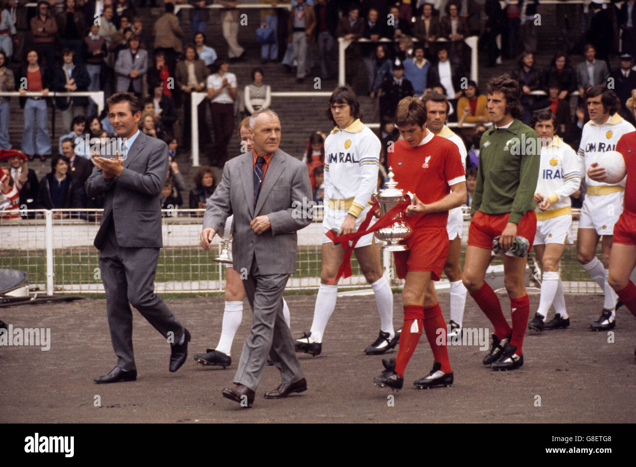 I due manager, Brian Clough (l) di Leeds United e Bill Shankly (secondo l) di Liverpool, guidano le loro squadre prima della partita. Seguono i due capitani, Billy Bremner di Leeds United (dietro Shankly) e Emlyn Hughes di Liverpool (quarto l), portando i trofei vinti dalle loro squadre nella stagione precedente. Si vedono anche David Harvey (terzo l), Paul Reaney (quinto r), Johnny Giles (terzo r) e Norman Hunter (secondo r), e Ray Clemence (quarto r) e Alec Lindsay (r) di Liverpool Foto Stock