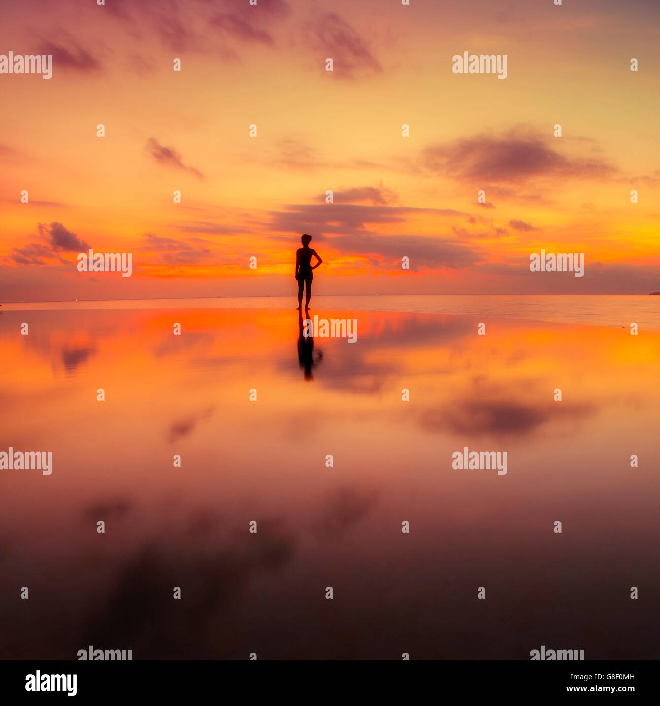 Una singola figura in piedi contro un caldo tramonto su una piscina infinity Foto Stock
