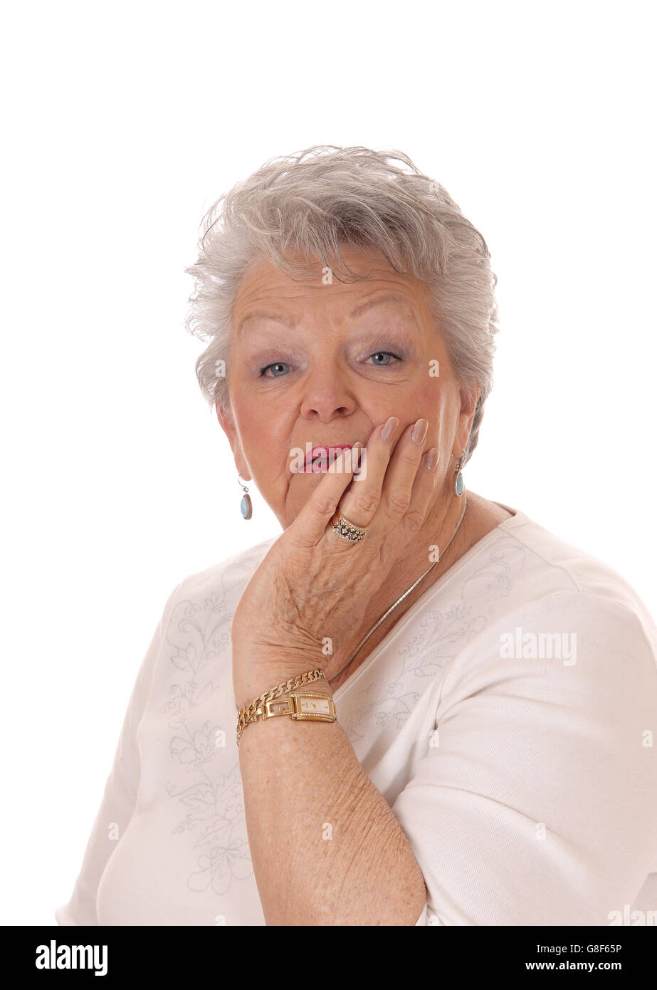 Una bella donna senior nei suoi anni settanta tenendo la sua faccia in mano e guardando sorpreso, isolato per sfondo bianco. Foto Stock