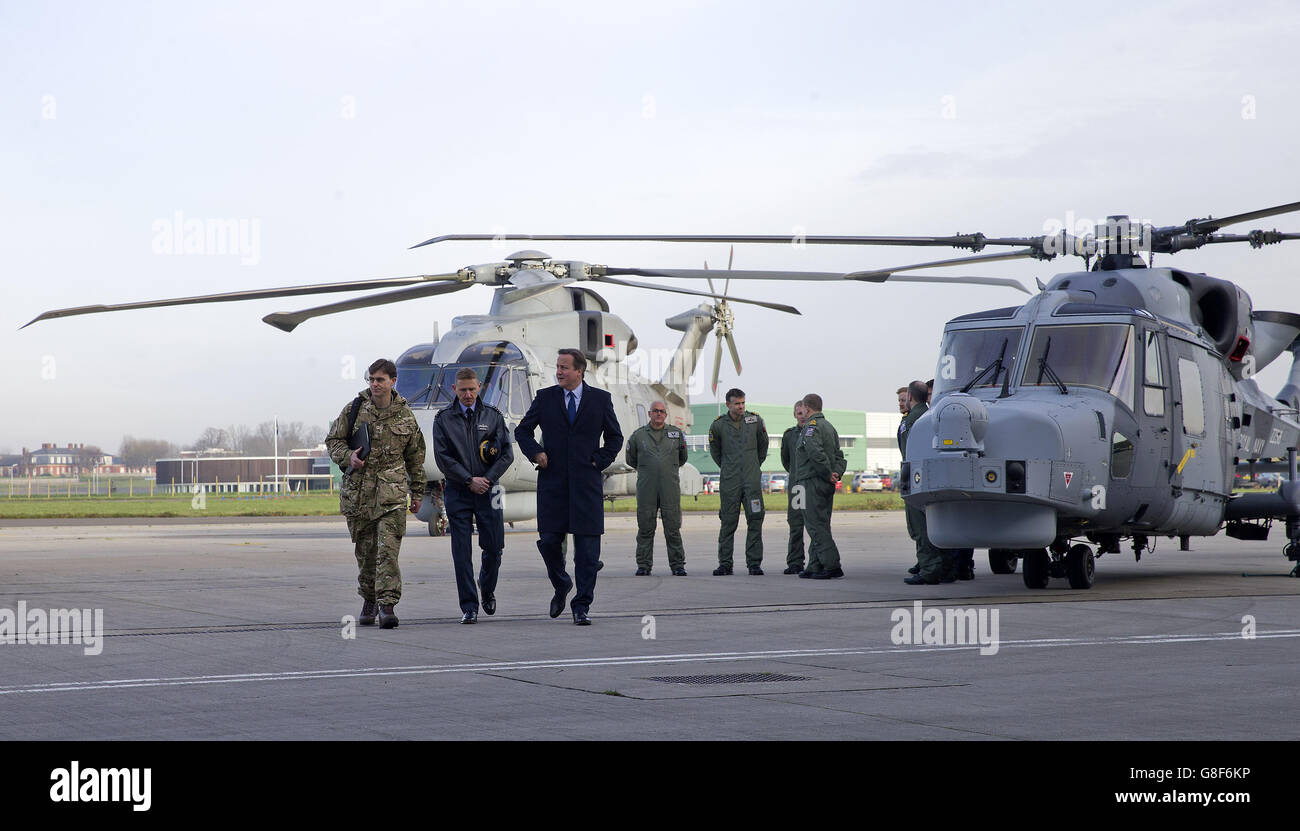 Il primo ministro britannico David Cameron (a destra) parla con il capitano del gruppo David Manning (al centro) mentre cammina davanti a un elicottero Royal Navy Merlin (a sinistra), E un elicottero multi-ruolo Royal Navy Wildcat, durante la sua visita alla stazione dell'aeronautica reale RAF Northolt, nella parte ovest di Londra, davanti alla Strategic Defense and Security Review (SDSR) del suo governo. Foto Stock