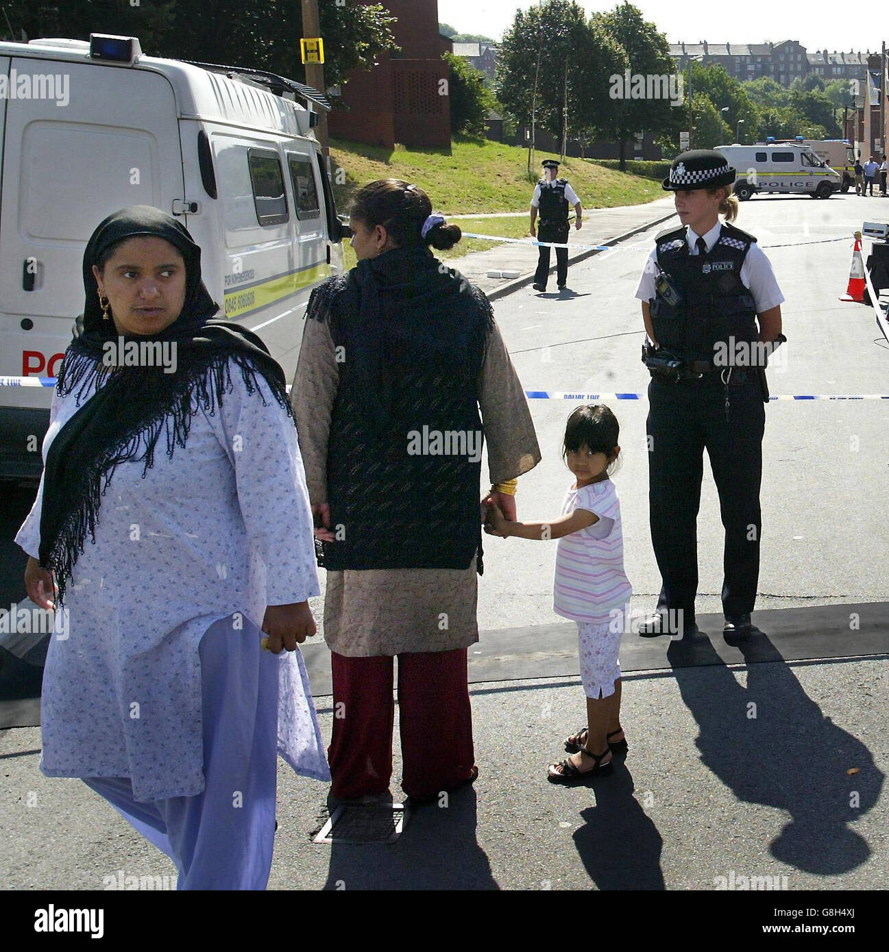 Un poliziotto che presienta un cordone parla con la gente locale incapace di ritornare nelle loro case nella zona di Hyde Park di Leeds. Foto Stock