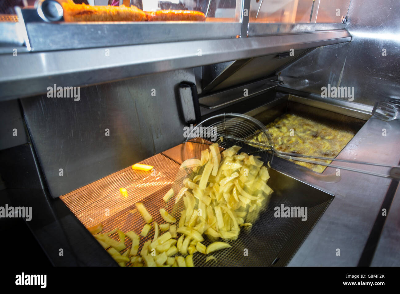 La cottura di chip in un pesce e chip shop con pentole di grasso bollente, adnd un chip scoop. Foto Stock
