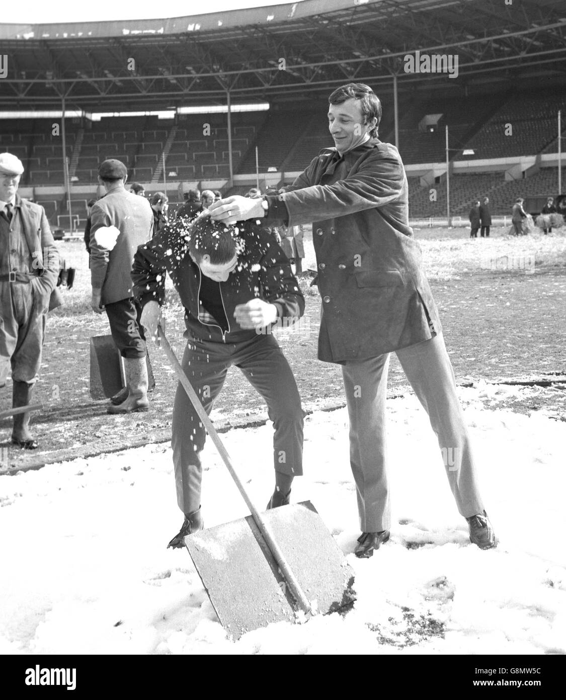 Mike Summerbee di Manchester City, con Ted Gromnicki di Kingsbury, Londra, una delle squadre che sgomberano la neve dal campo al Wembley Stadium. Insieme al manager Joe Mercer, i giocatori di Manchester City hanno dato un'occhiata all'arena della viniera, dove domani saranno chiamati a incontrare West Bromwich Albion nella finale della Coppa di Lega. Foto Stock