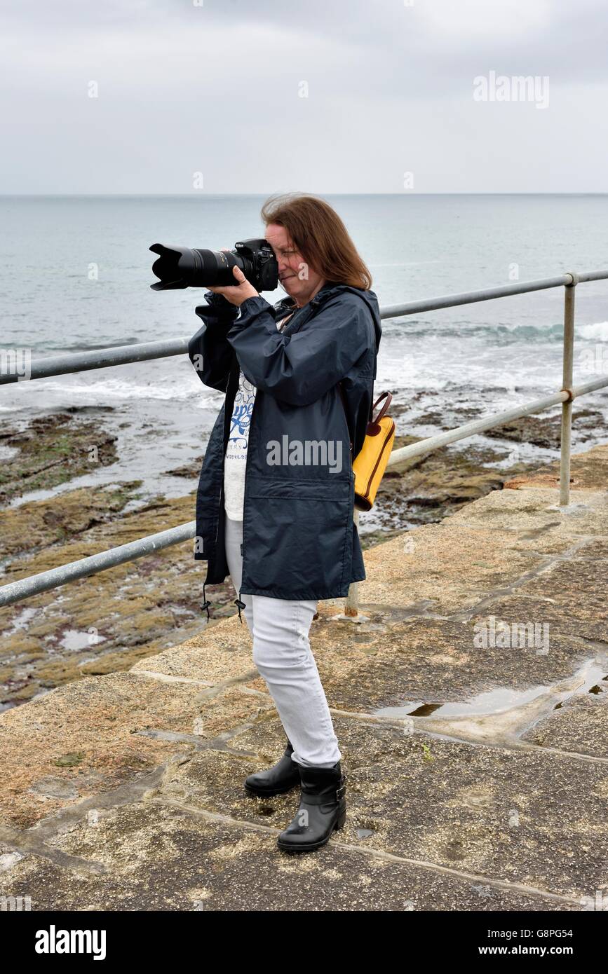 Una femmina di fotografo utilizzando la fotocamera reflex digitale con un teleobiettivo con zoom in Porthleven Cornwall Inghilterra REGNO UNITO Foto Stock