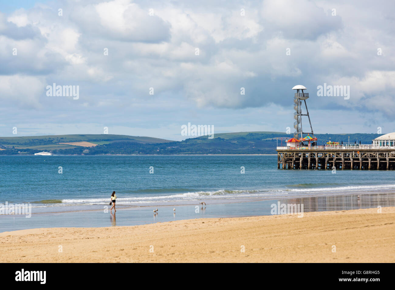 La donna a piedi lungo la spiaggia di Bournemouth con Pier e viste al Purbecks con Traghetti Condor in giugno Foto Stock