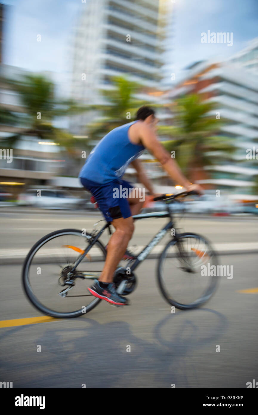 RIO DE JANEIRO - Marzo 6, 2016: un giovane brasiliano uomo cavalca la sua bicicletta in motion blur sulla spiaggia di Ipanema beachfront road. Foto Stock