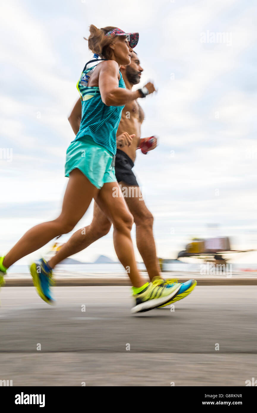 RIO DE JANEIRO - Aprile 3, 2016: una coppia di carioca jogging passano in motion blur sul fronte spiaggia di Ipanema pista ciclabile. Foto Stock
