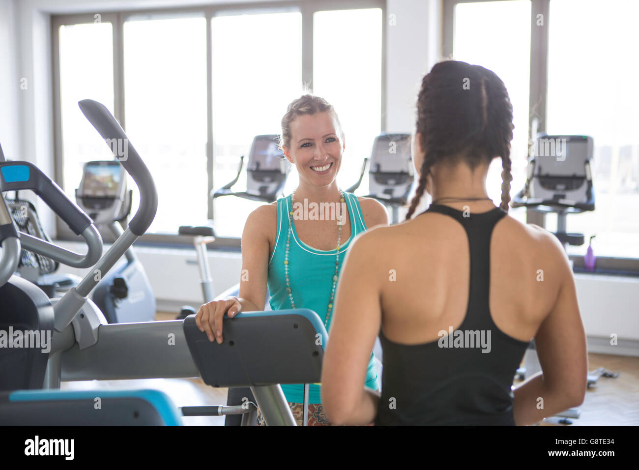 Istruttore di Fitness a parlare con una donna con attrezzature ginniche in background Foto Stock