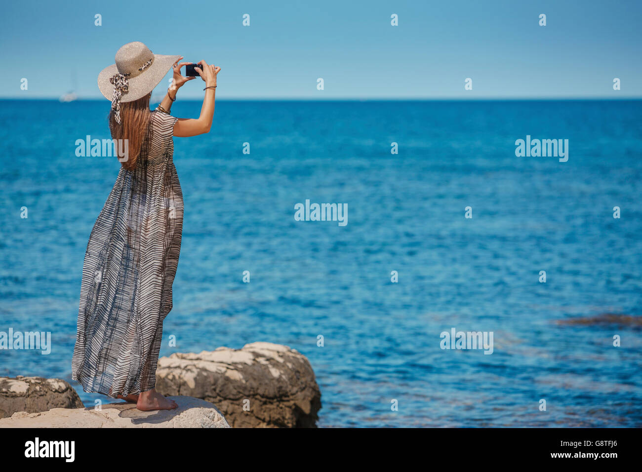 Bella donna con cappello per il sole di scattare una foto del mare Foto Stock