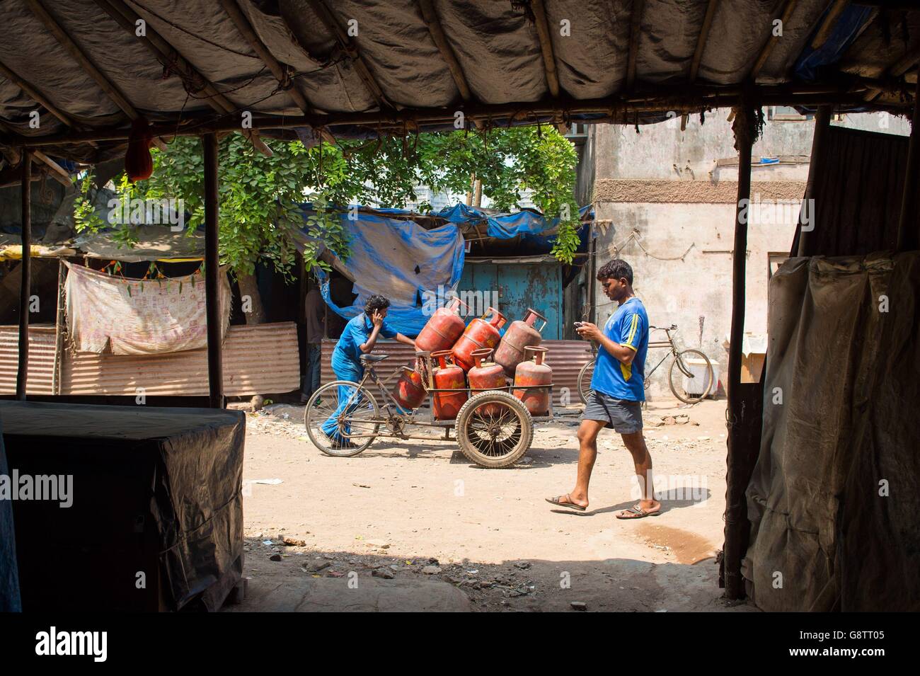 Un uomo spinge una moto carica di bombolette a gas per le strade della zona della baraccopoli di Ambedkar Nagar a Mumbai, India. Foto Stock
