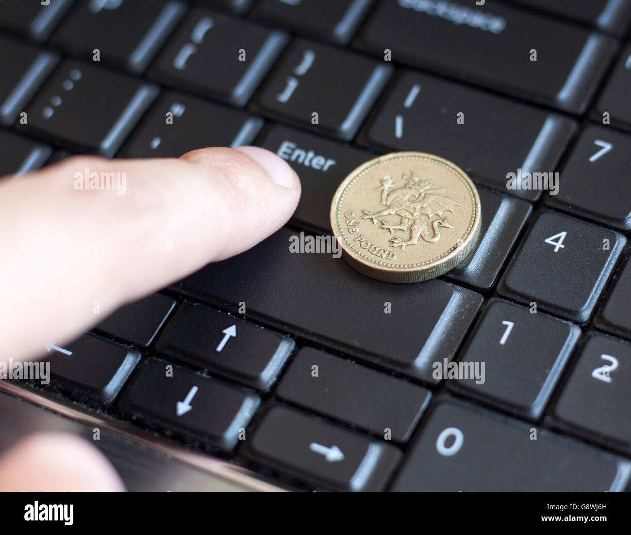 British una sterlina moneta giacente sulla tastiera del laptop con il dito premendo il tasto Invio Foto Stock