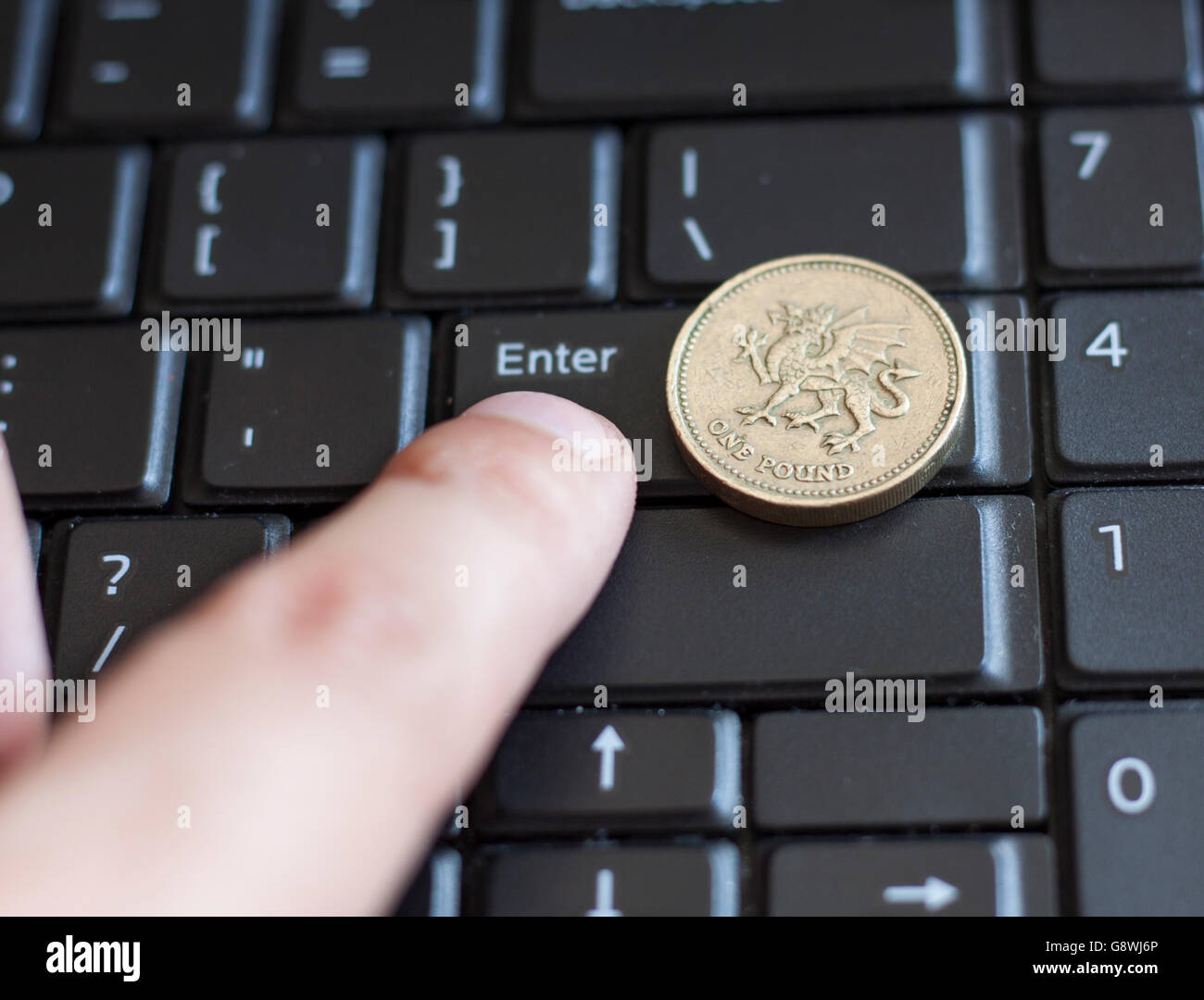 British una sterlina moneta giacente sulla tastiera del laptop con il dito premendo il tasto Invio Foto Stock