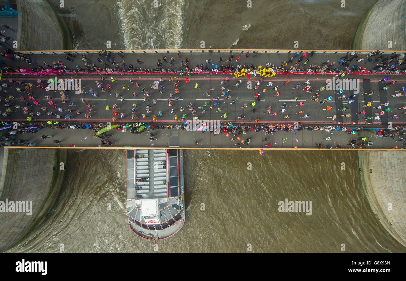 I corridori attraversano il Tower Bridge mentre una barca passeggeri passa sul Tamigi sotto durante la Maratona di Londra 2016 Virgin Money. Foto Stock