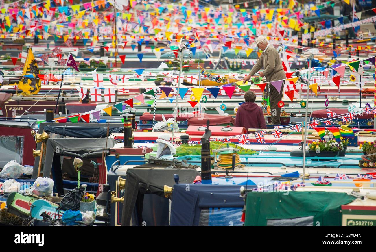 Un proprietario di una barca regola le bandiere sulla sua barca durante il festival annuale Canalway Cavalcade della Inland Waterways Association, a Little Venice, Londra, che dal 1983 ha caratterizzato un raduno di barche strette decorate che prendono parte a competizioni e sfilate. Foto Stock