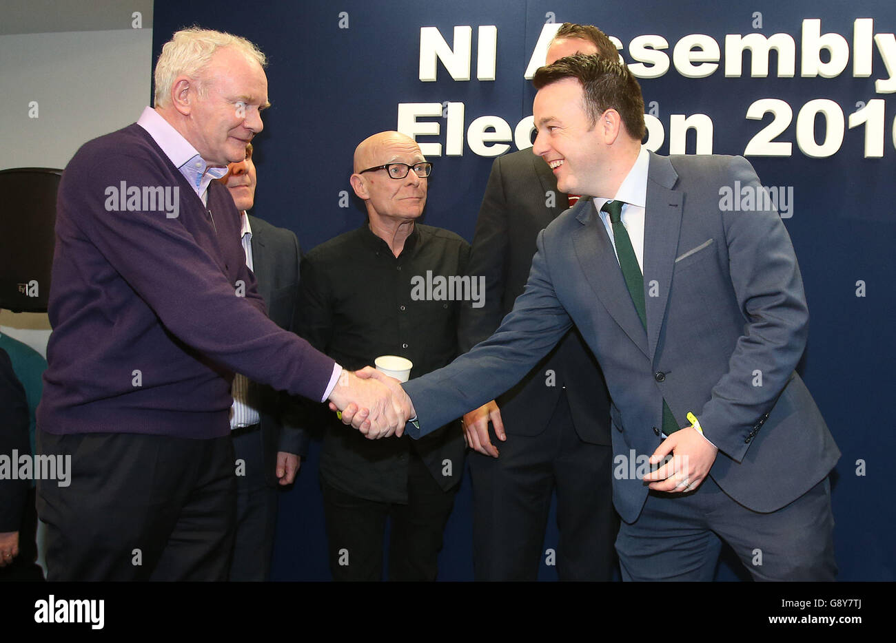 Martin McGuinness (Sinn Fein) stringe le mani con il Colum Eastwood (SDLP) mentre Eamonn McCann (persone prima del profitto) guarda al centro dopo la loro elezione, come il conteggio dei voti continua alla Foyle Arena di Londonderry nelle circoscrizioni di Foyle e di Londonderry Est nelle elezioni dell'Assemblea dell'Irlanda del Nord. Foto Stock