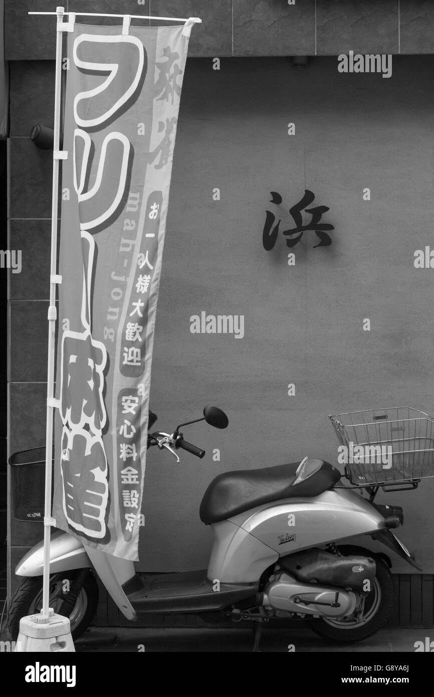 Un ciclomotore si nasconde dietro a mah-jong banner al di fuori di un modesto edificio in Mitaka, Tokyo, Giappone. Foto Stock