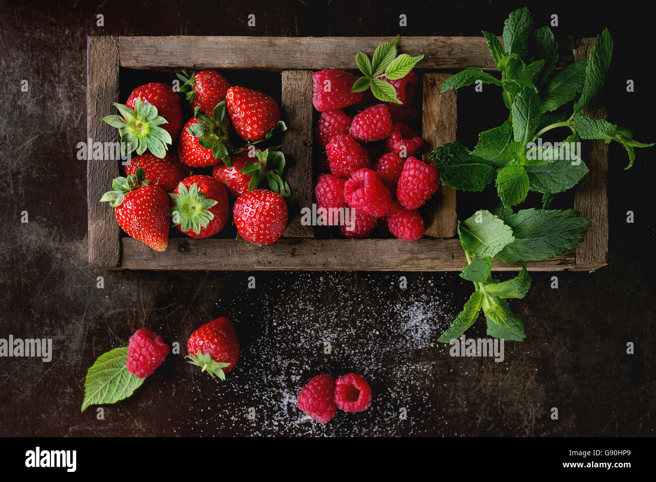 Frutti di bosco freschi fragola e lampone con mazzetto di menta in vecchio legno scatola sezionata su testurizzato scuro dello sfondo. Vista dall'alto. W Foto Stock