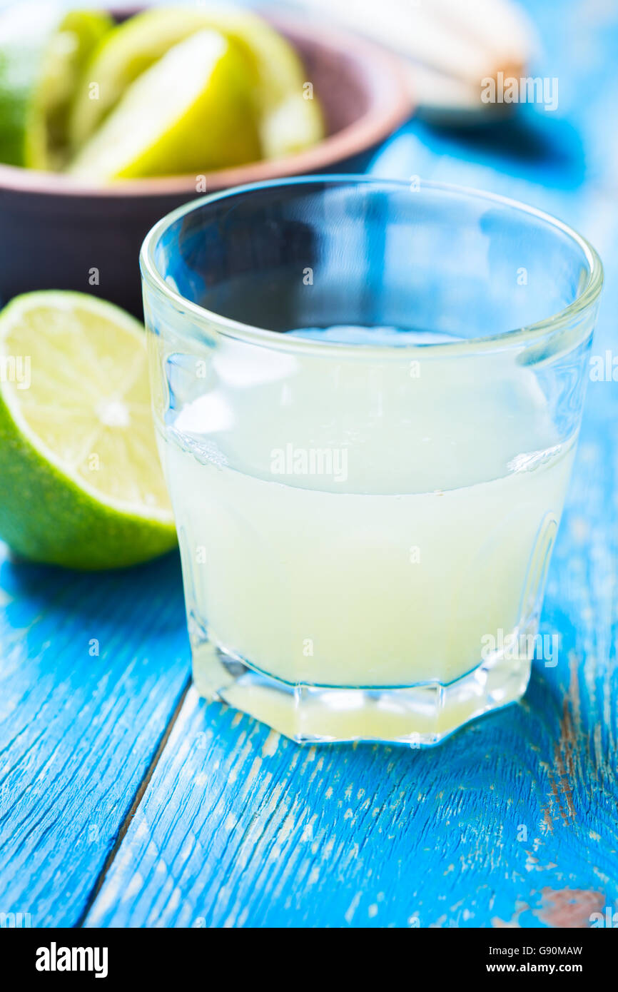 Vetro con succo di lime fresco e lime fresco blu su sfondo di legno Foto Stock