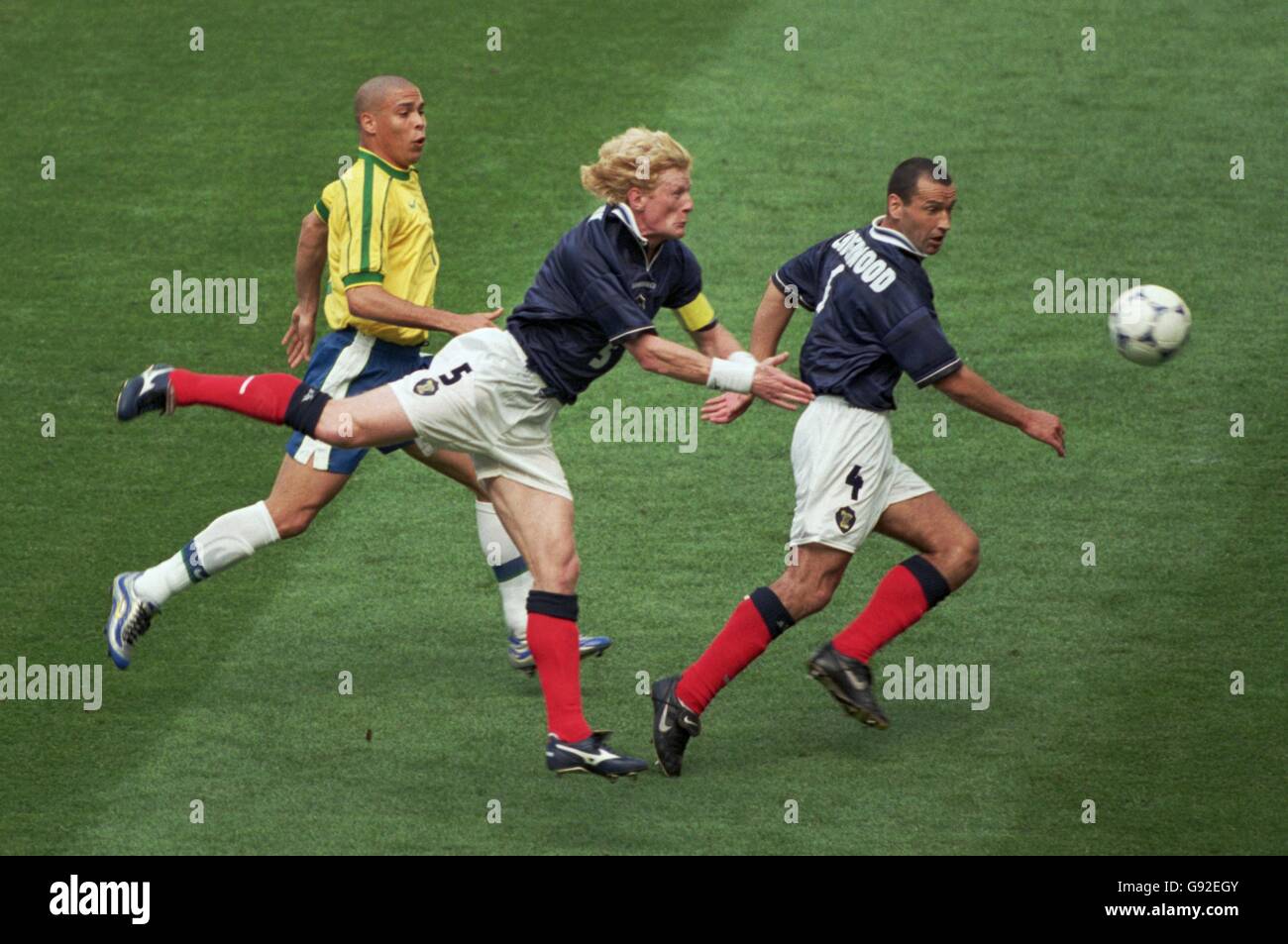 Il Colin Hendry (centro) della Scozia dirige la palla oltre il suo Obiettivo come Ronaldo del Brasile (a sinistra) e Colin Calderwood di Scozia (a destra) guardare sopra Foto Stock