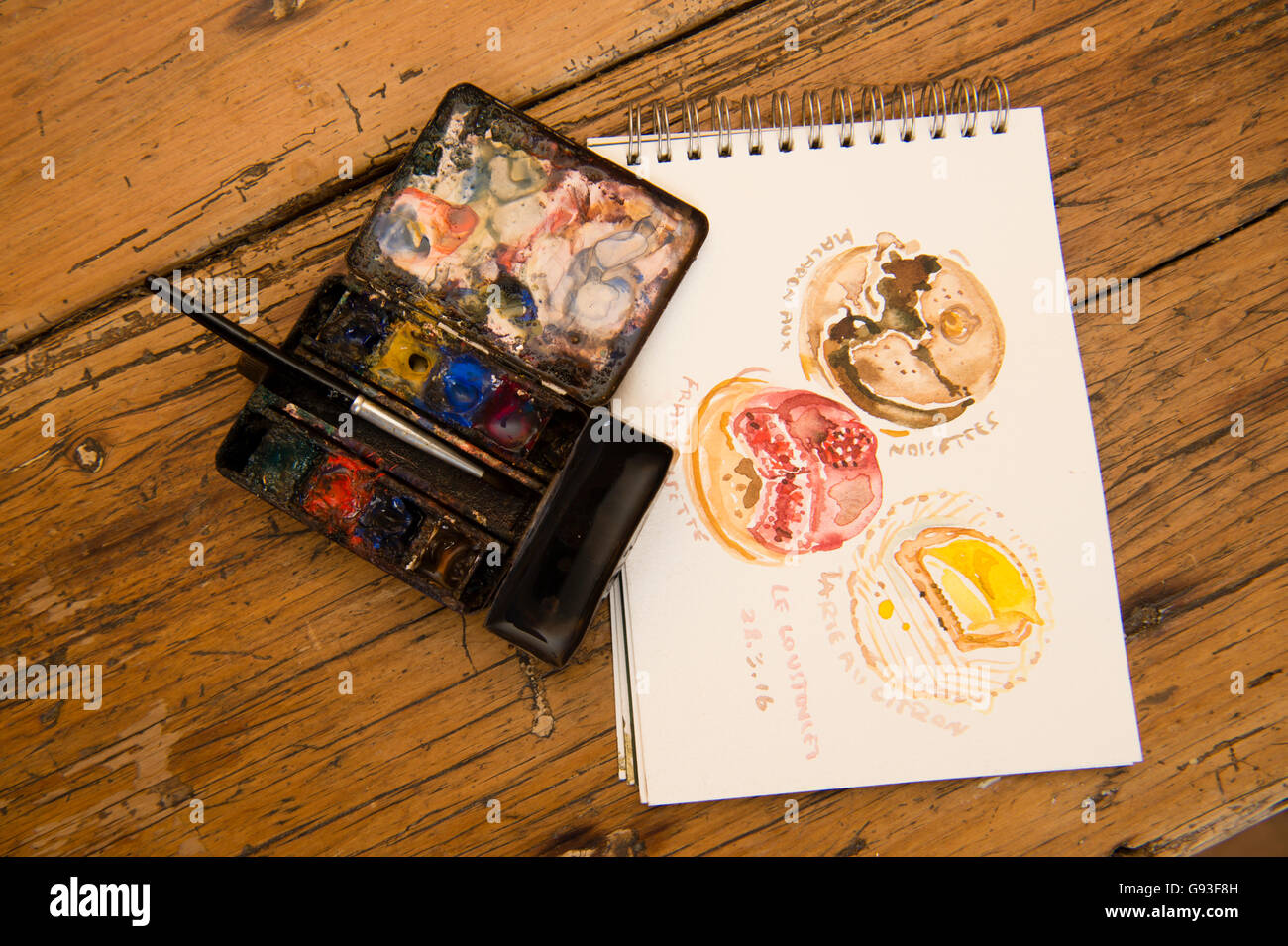 Un piccolo ben utilizzati acquerello artista della casella di viaggio di vernici e sketch pad con piccoli dipinti di articoli di cibo, REGNO UNITO Foto Stock