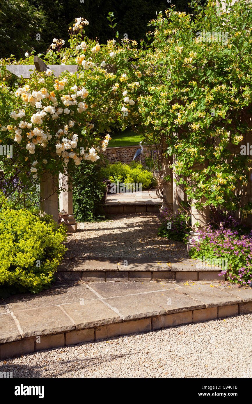 Regno Unito. Un giardino arch con rose e caprifoglio e patio al di là. Foto Stock