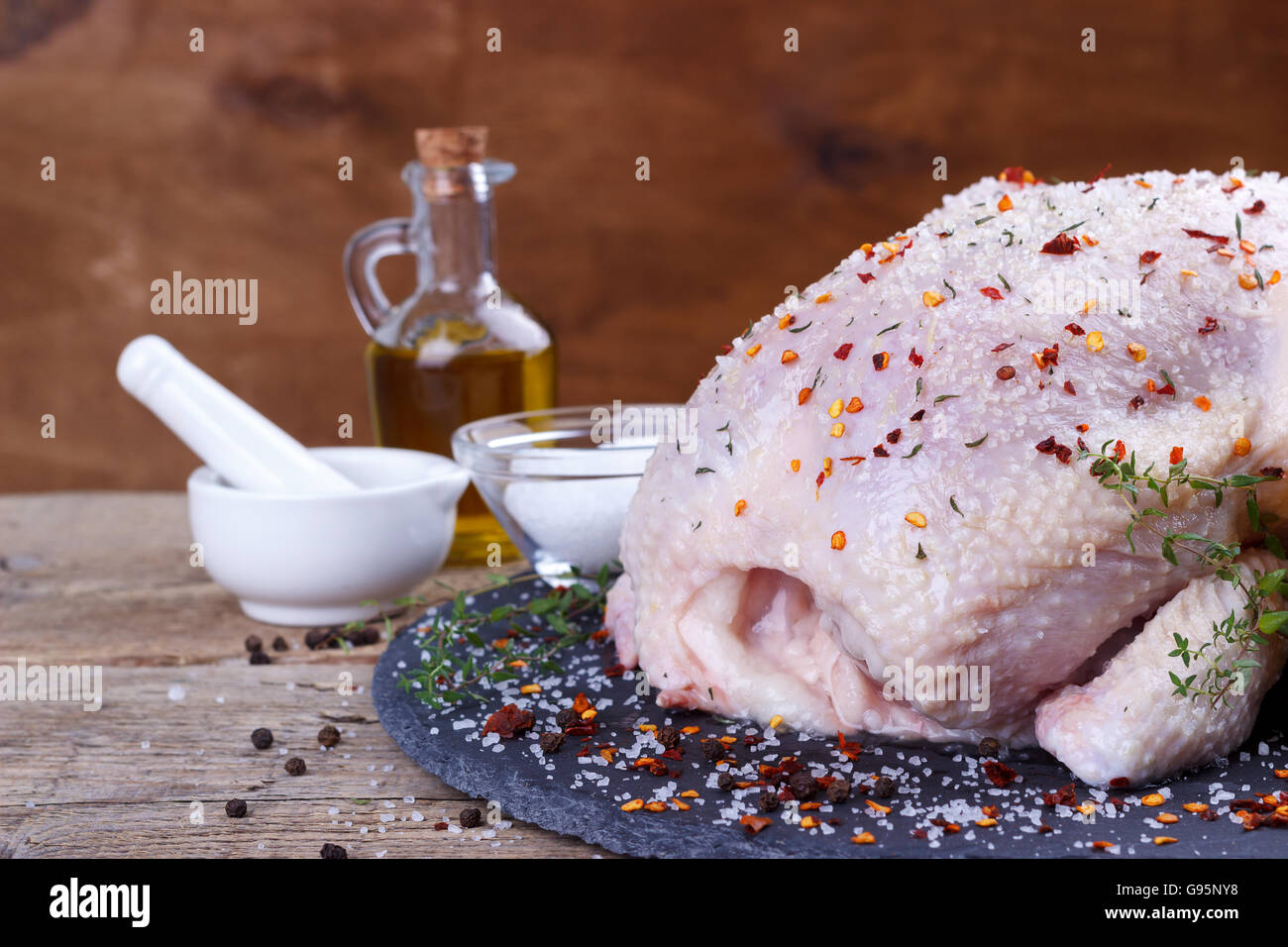 Tutto il pollo crudo con limone,timo,paprika sale e pepe spezie sulla pietra nera tagliere.Il fuoco selettivo Foto Stock