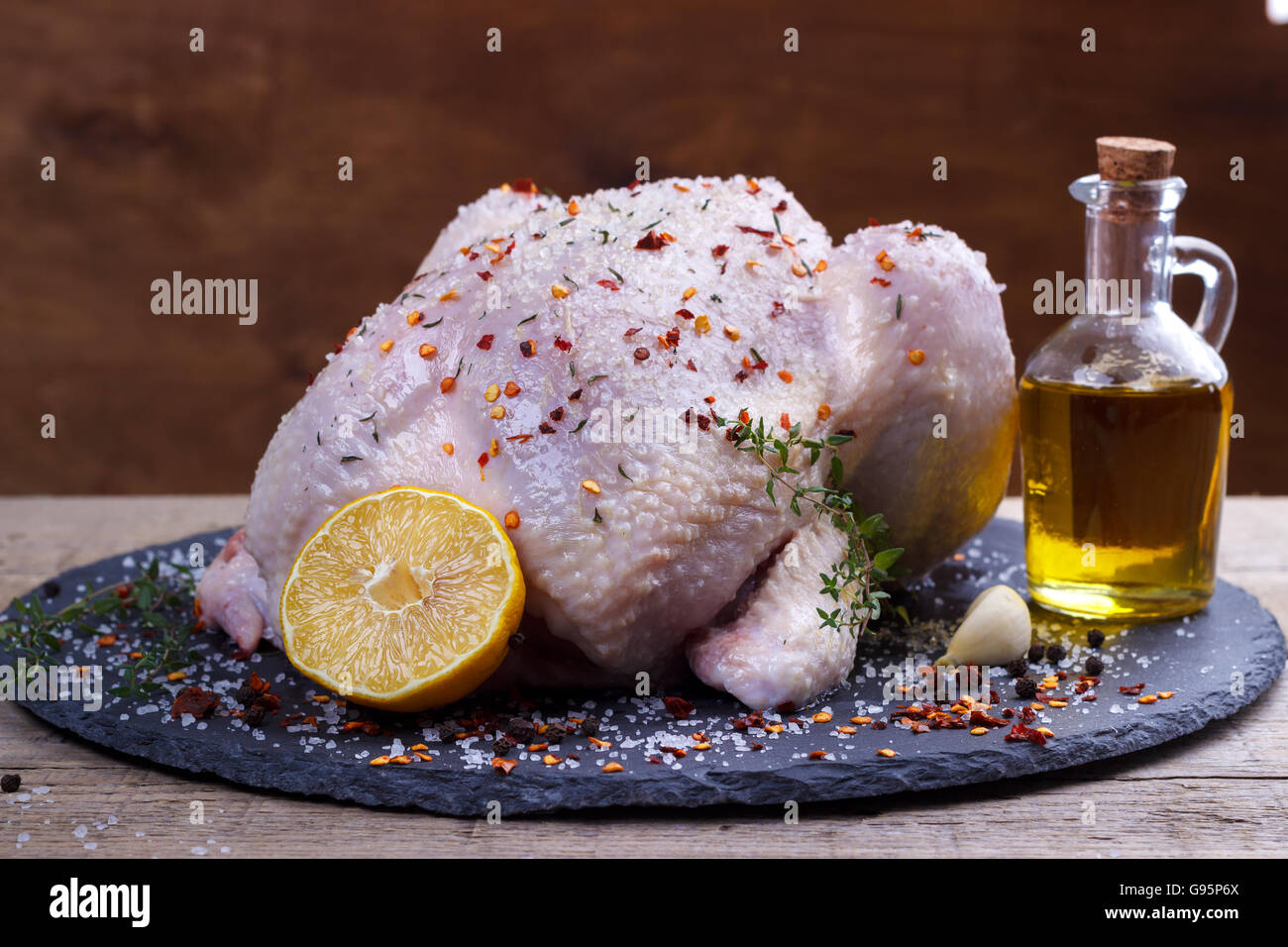 Tutto il pollo crudo con limone,timo,paprika sale e pepe spezie sulla pietra nera tagliere.Il fuoco selettivo Foto Stock