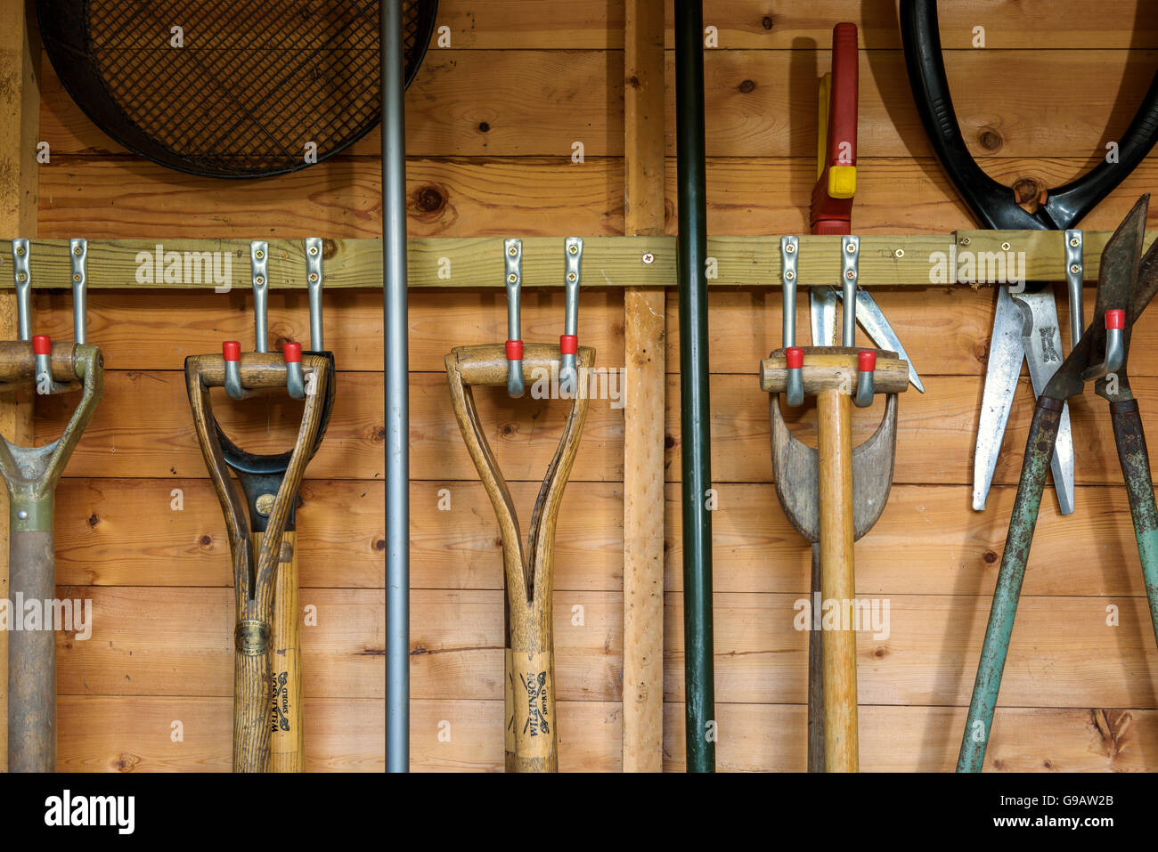 Attrezzi da giardino appese in un capannone di legno. Foto Stock
