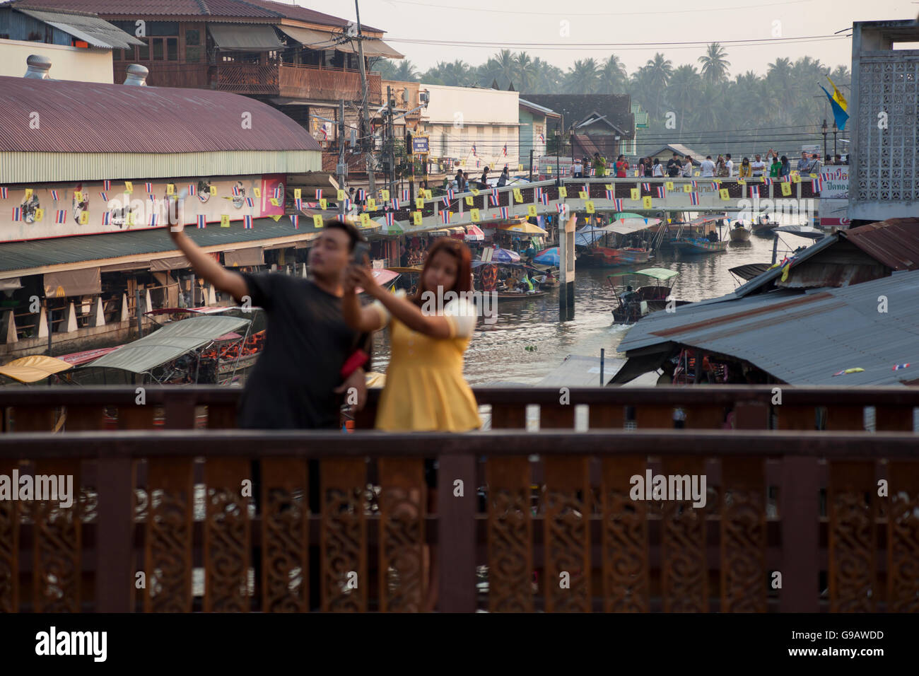 Un paio di prendere un selfie di se stessi in piedi su un ponte che si affaccia sul mercato galleggiante in Maeklong in Thailandia. Foto Stock