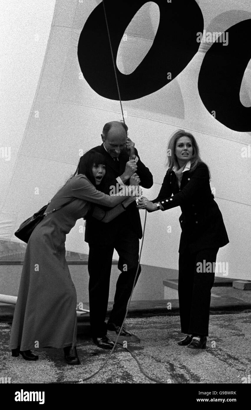 Le cerimonie di bandiera sono solitamente lasciate a flunkeys ma oggi (lunedì) M. Rene Keller, ambasciatore svizzero, ha prestato una mano e ha aiutato a sollevare lo standard 007 sopra il centro svizzero in Coventry Street, Londra, WC1. Aveva due assistenti attraenti - Bond Girls Mona Chong da bangkok (sinistra) e Jpanna Lumley di Londra. Foto Stock