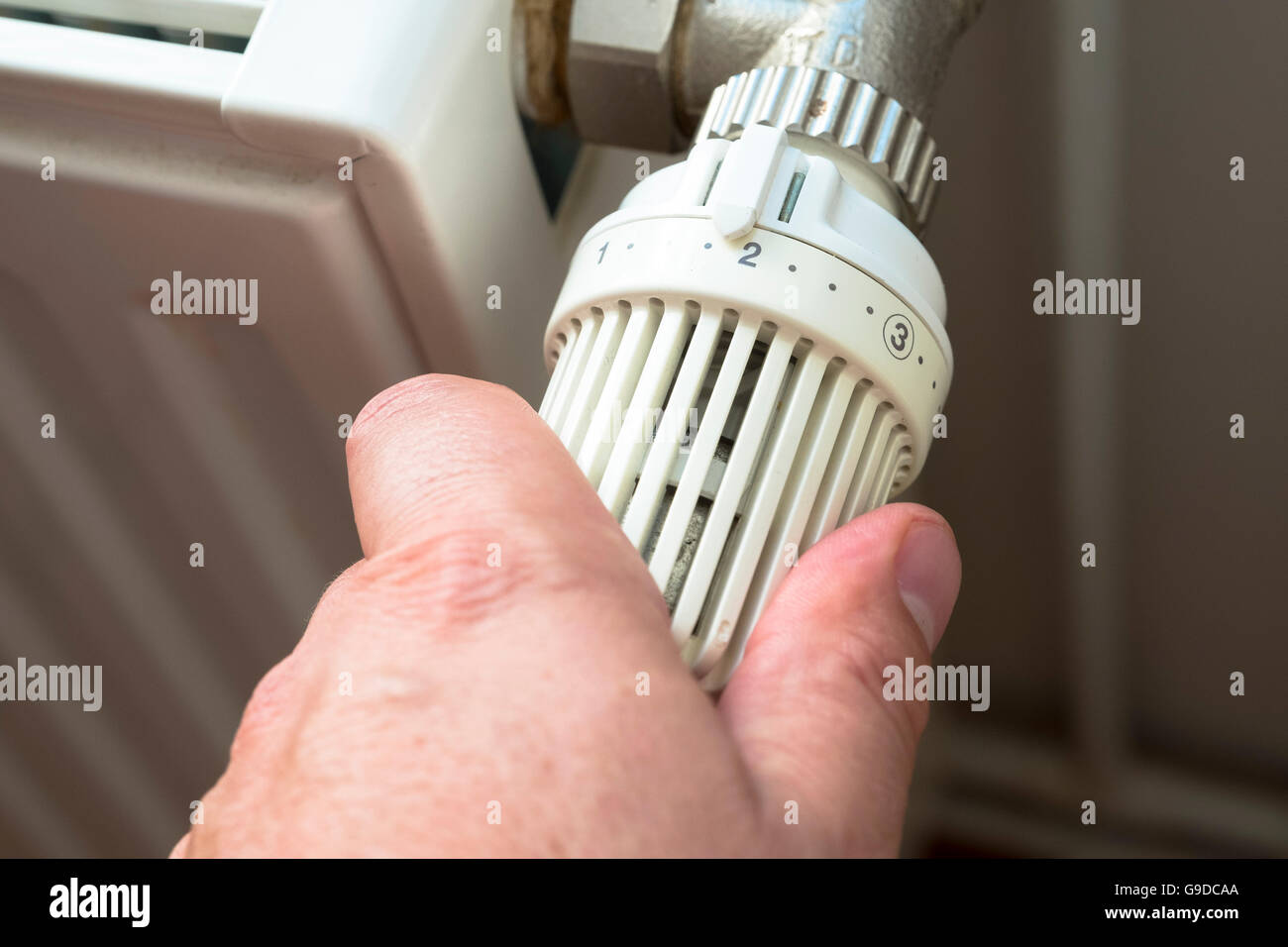 L'uomo ruotando verso il basso il termostato sul gas powered centrale del radiatore di riscaldamento per risparmiare energia Foto Stock