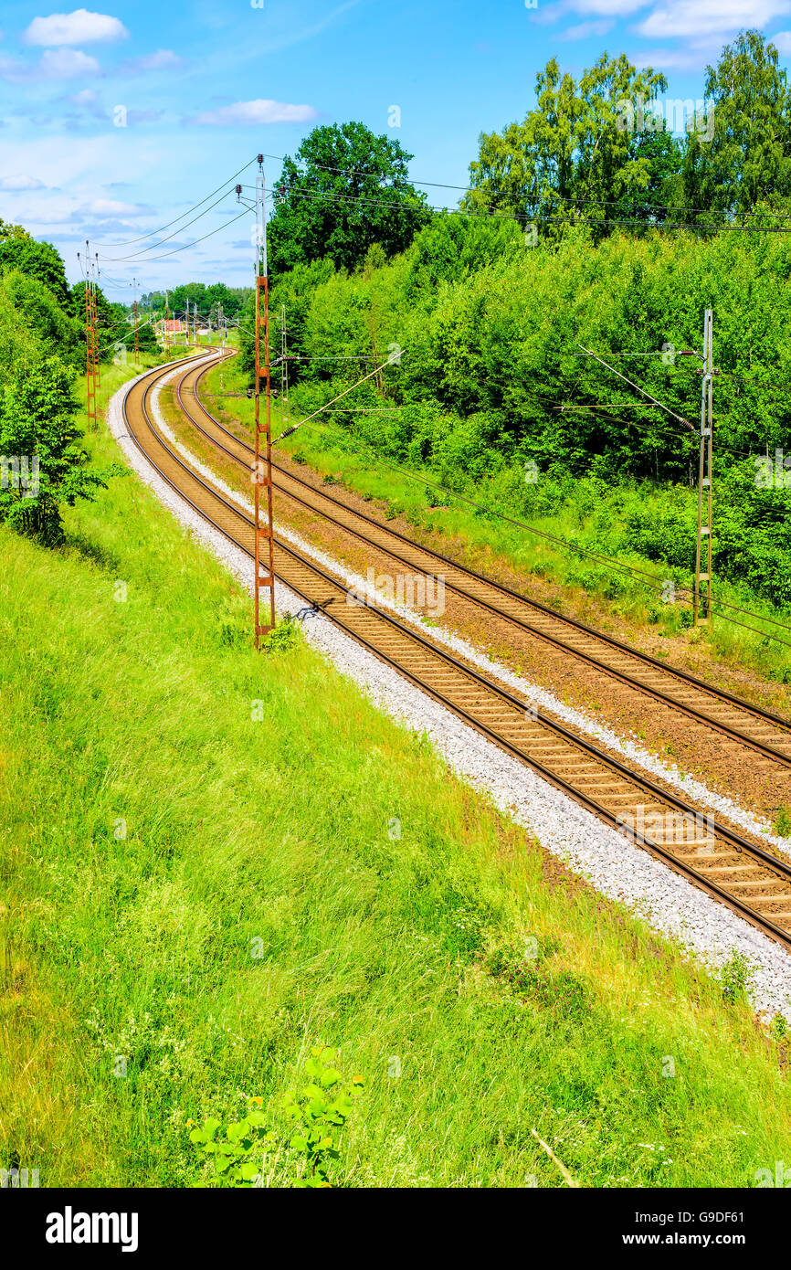 Incantevole tratto di ferrovia sul paesaggio con case lontane e lussureggiante vegetazione lungo i lati. Foto Stock