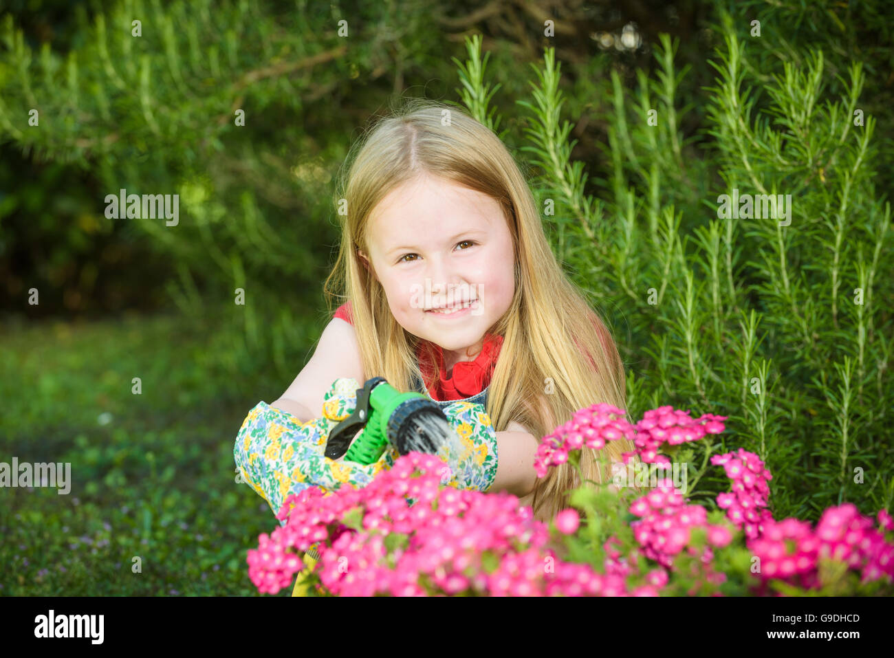 Bella ragazza bionda fiori di irrigazione, prato su una soleggiata giornata splendida davanti alla casa. Foto Stock