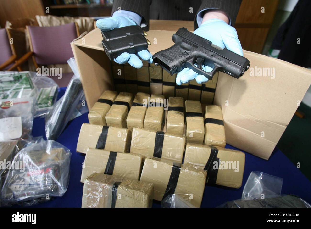 Un membro del Garda la criminalità organizzata l'unità visualizza un Glock pistola automatica e due riviste caricato al di sopra di una grande partita di armi e di 8 milioni di euro di eroina sequestrata in incursioni separata nelle contee di Meath e Dublino. Picture Data: domenica 25 giugno 2006. Foto Stock