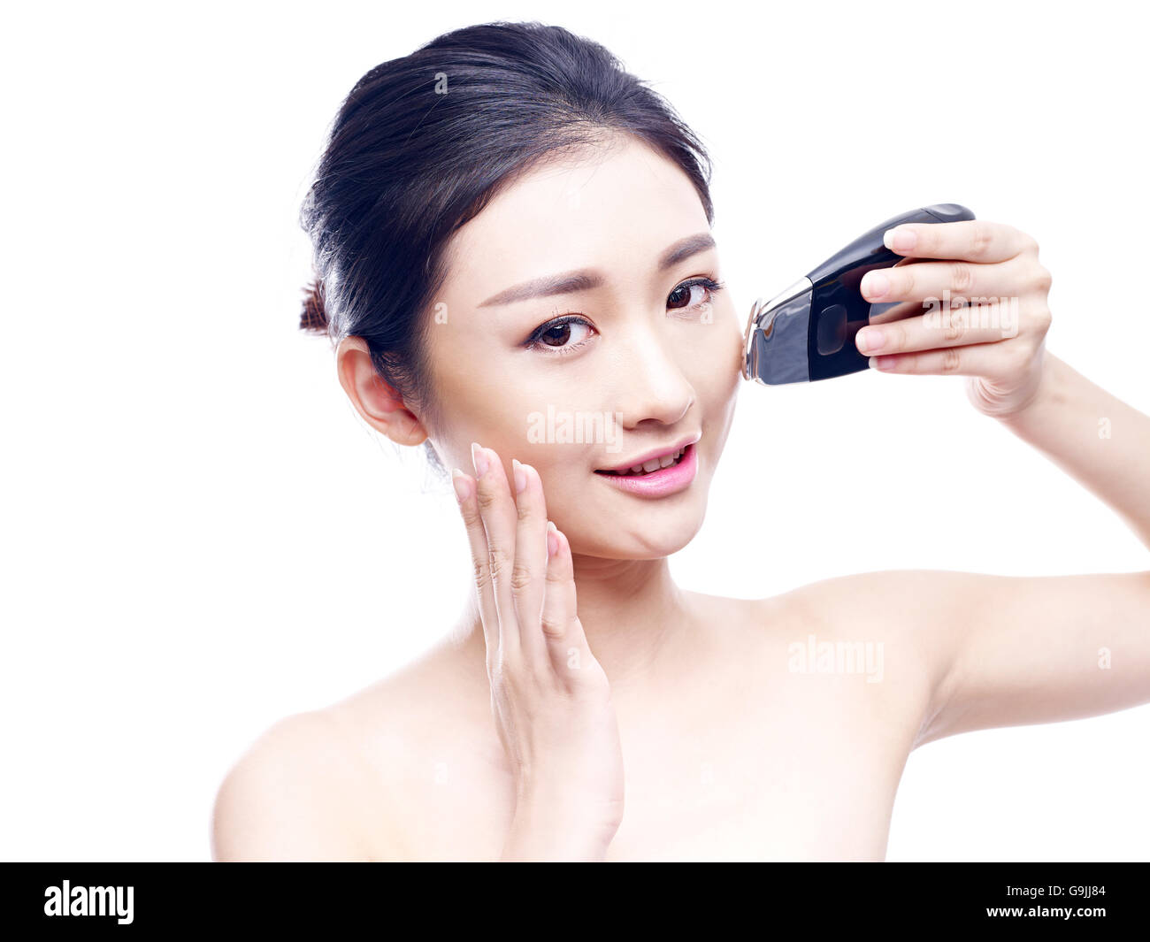 Giovane donna asiatica utilizzando una faccia strumento spa, isolato su bianco. Foto Stock