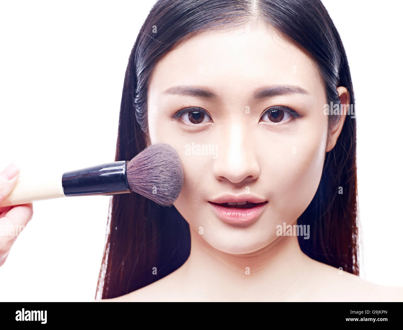 Make-up foundation spazzolato sulla faccia di una giovane e bella modello asiatico, isolato su sfondo bianco. Foto Stock