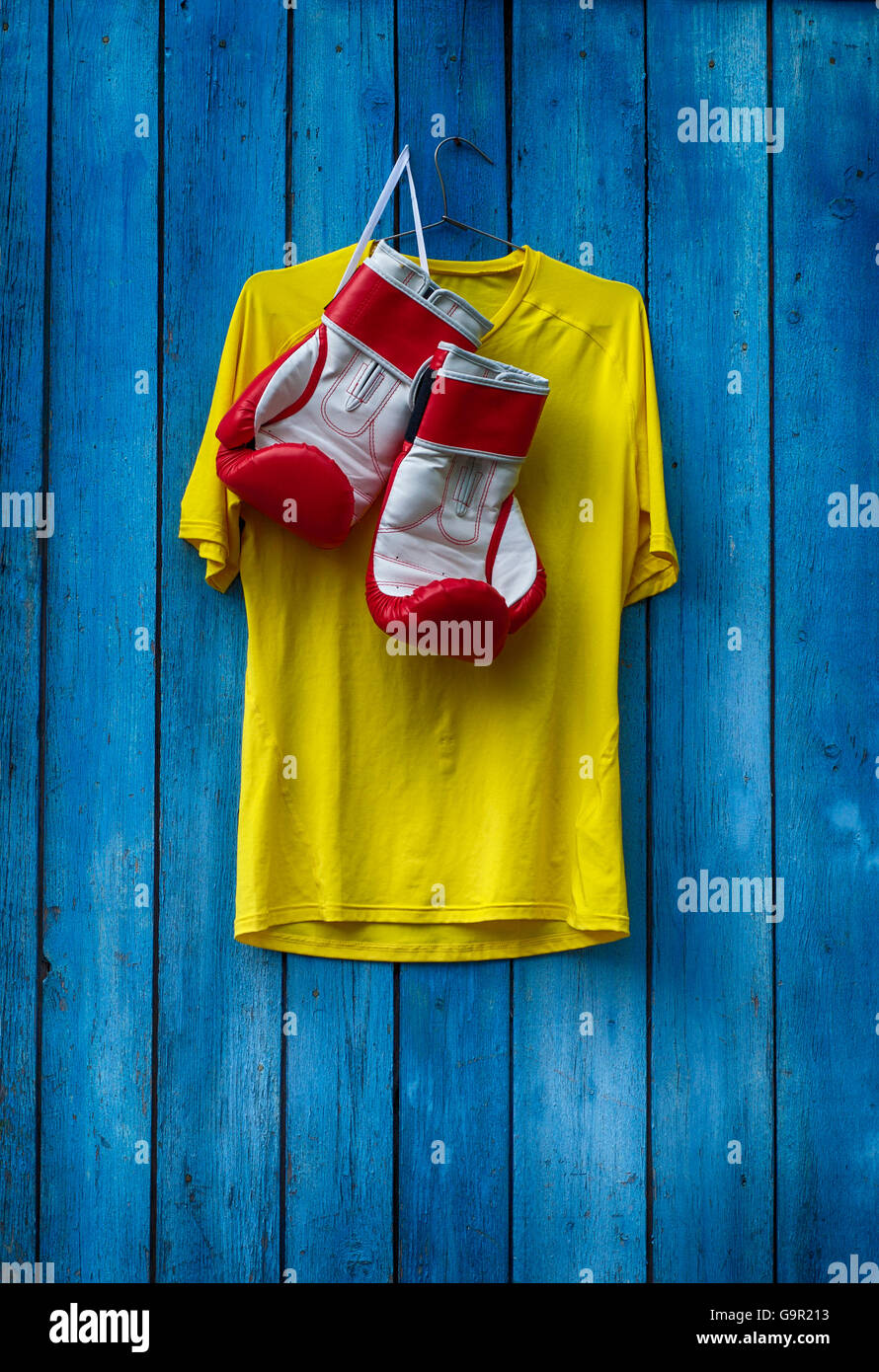 Giallo T-shirt e i guantoni appesi su una tavola di legno vecchio muro blu Foto Stock