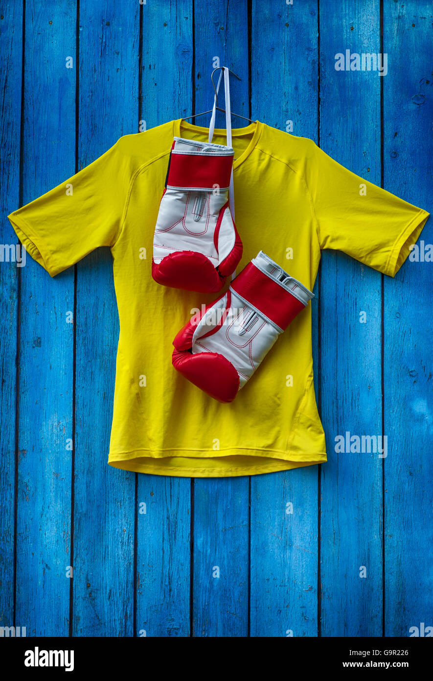 Giallo T-shirt e i guantoni appesi su una tavola di legno vecchio muro blu Foto Stock